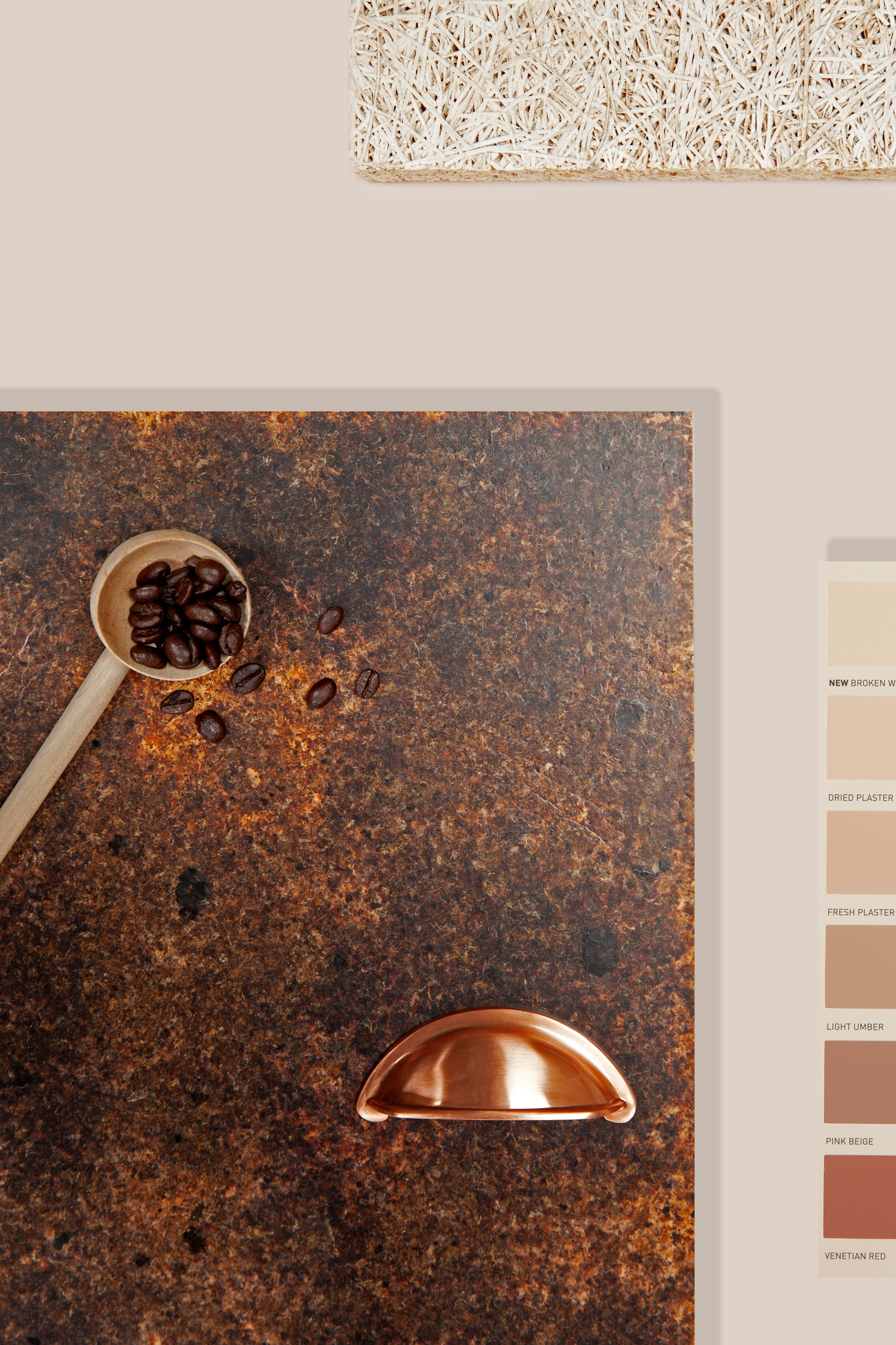 A mood board of a Kava husk sample. Next to it shows part of a colour chart with soft warm red toned whites to brown to red. On top of the sample sits a wooden spoon with coffee beans in and slightly spilled over. A copper door handle also sits on the sample. Above the husk kava sample is a hemp material sample. The background is a soft warm red-white.