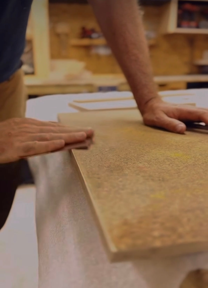 A close up of a sheet of KAVA Peach being sanded in the workshop. Image shows two hands sanding the edge of the board with a piece of sandpaper.