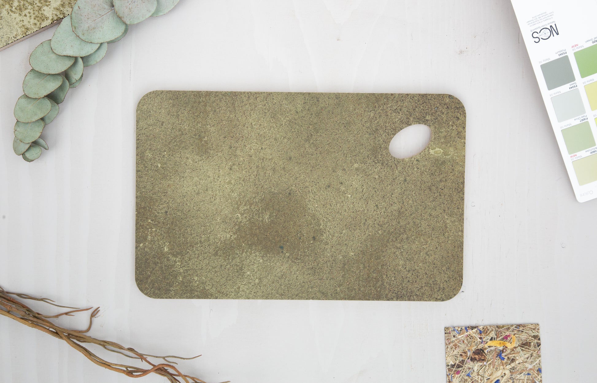A close up of a KAVA tray, made by pressing coffee waste and brass into birch plywood. The corners are rounded at a soft radius and one corner is an oval shaped hole so you can hold the tray with your thumb, or hang it on a hook.