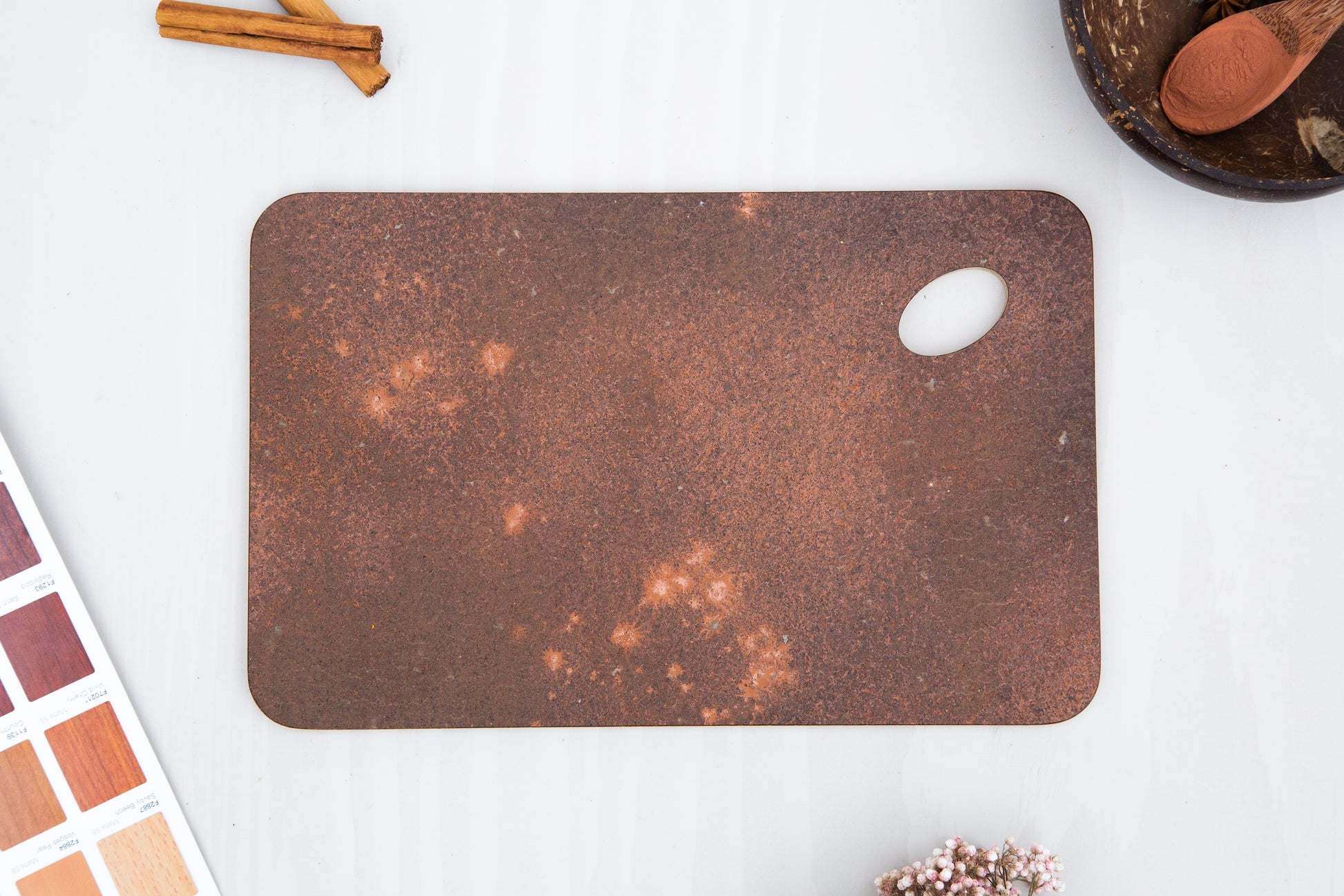 A close up of a KAVA tray, made by pressing coffee waste and copper into birch plywood. The corners are rounded at a soft radius and one corner is an oval shaped hole so you can hold the tray with your thumb, or hang it on a hook.