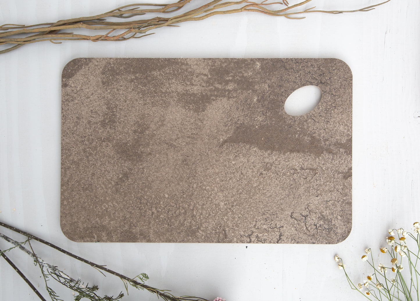 A close up of a KAVA tray, made by pressing coffee waste and bronze into birch plywood. The corners are rounded at a soft radius and one corner is an oval shaped hole so you can hold the tray with your thumb, or hang it on a hook.